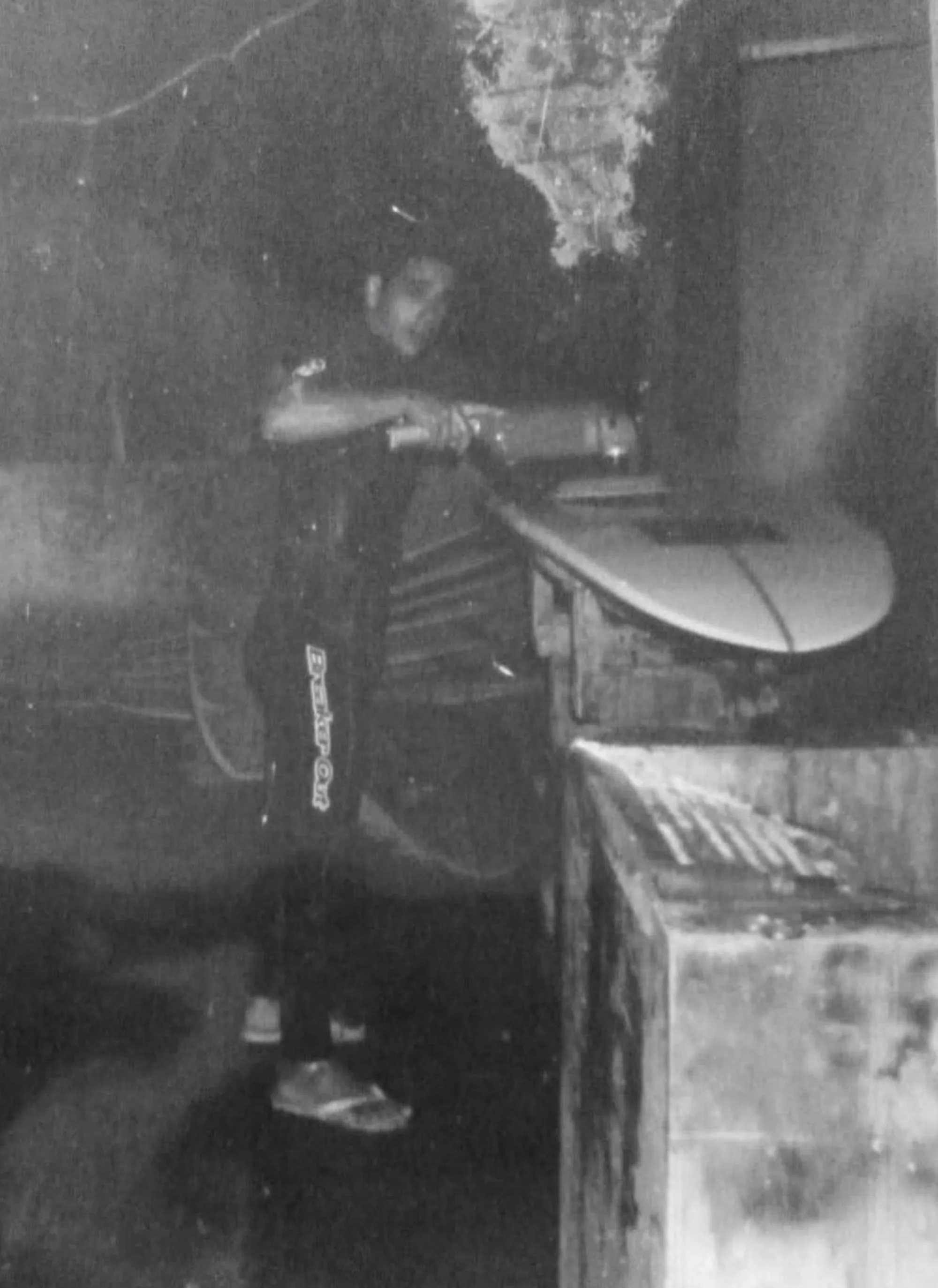 Alessandro Pierre jeune shapant une planche de surf dans un atelier rudimentaire au Brésil, photo noir et blanc
