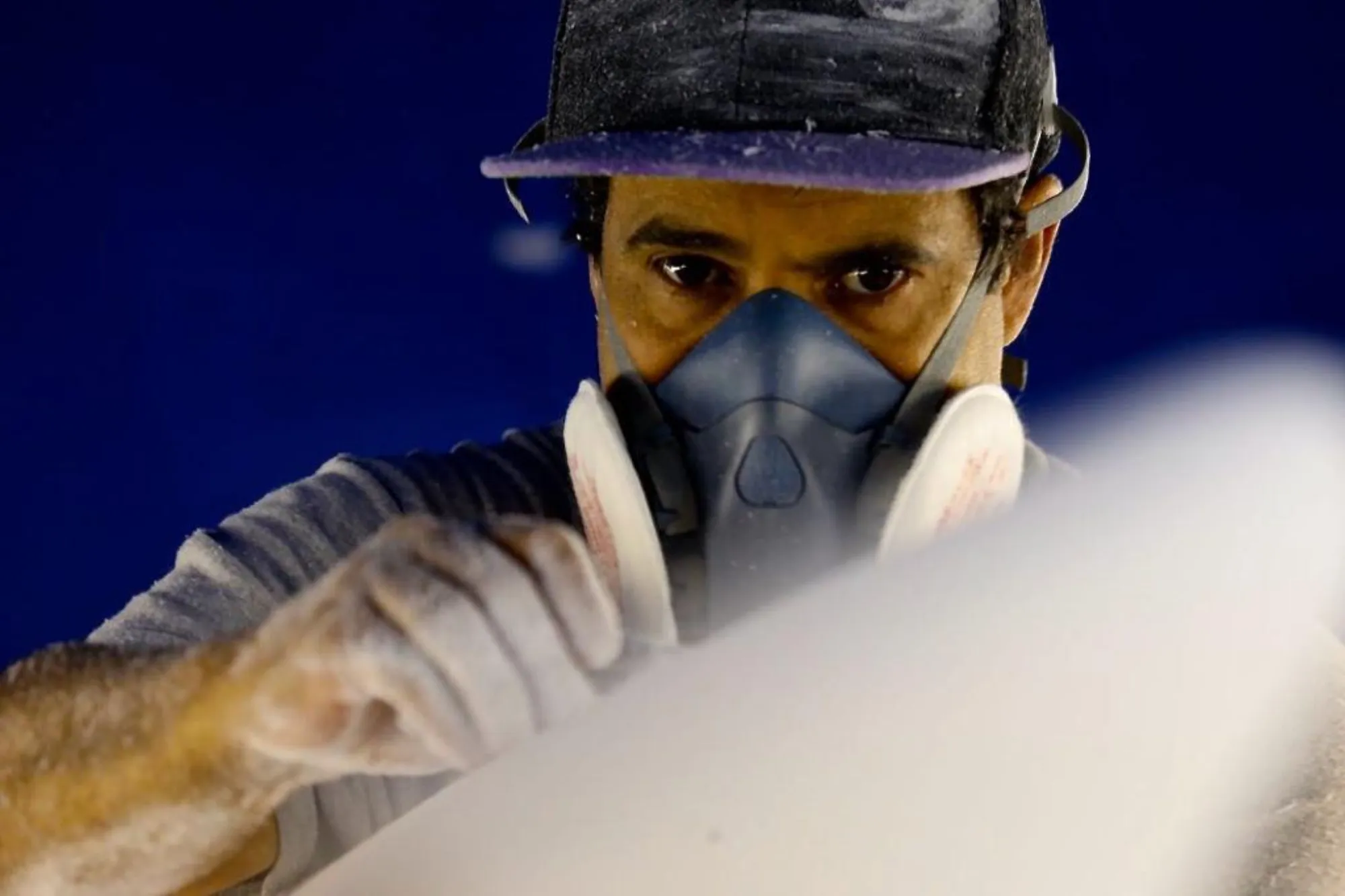 Alessandro Pierre shapant une planche de surf avec masque de protection dans son atelier de Seignosse