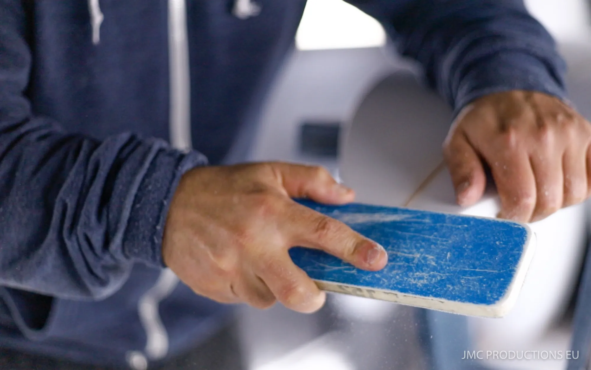 Mains d'Alessandro Pierre ponçant le rail d'une planche de surf avec une cale bleue